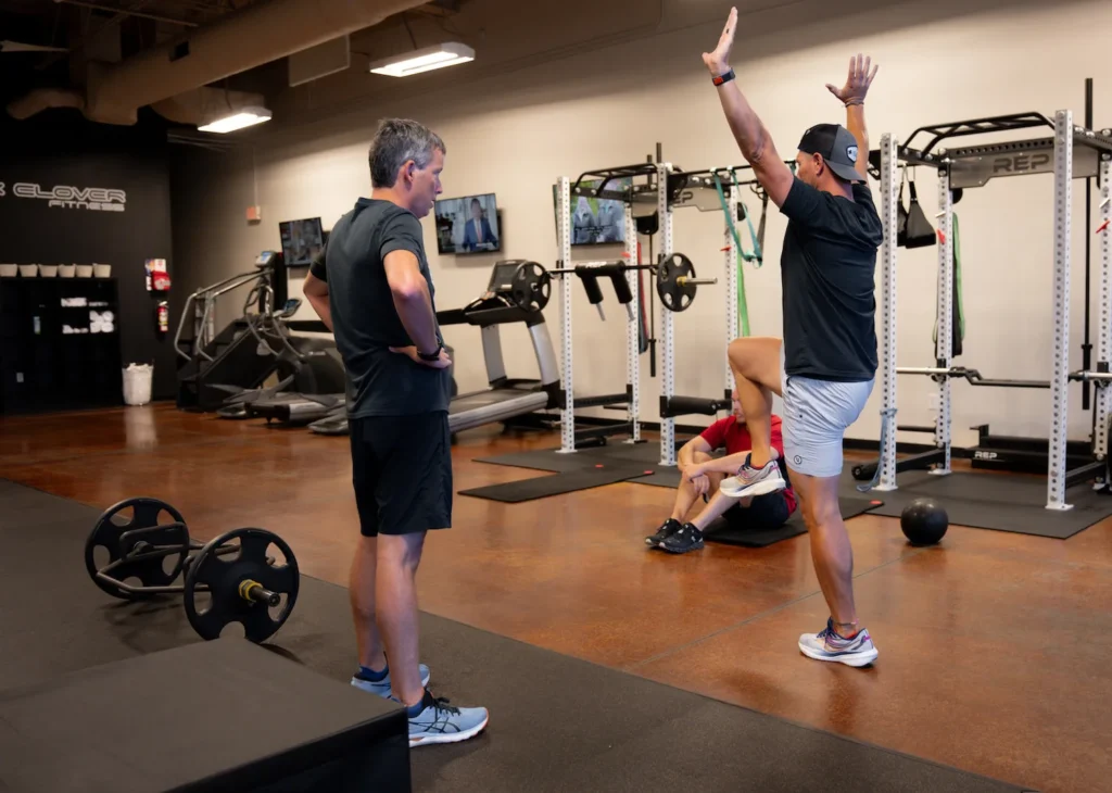 Personal trainer demonstrating a fitness exercise to clients in a well-equipped gym at Black Clover Fitness, emphasizing personalized training and community support for active adults.