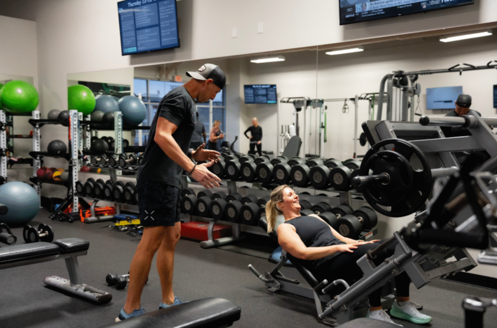 Personal trainer assisting a woman with a leg press exercise in a modern gym setting, emphasizing strength training for GLP-1 users to maintain muscle mass and metabolic health.