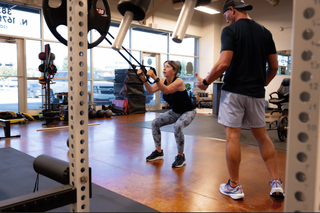 Woman performing strength training exercise with resistance bands under guidance of fitness trainer in gym, emphasizing muscle preservation for weight loss and metabolic health.